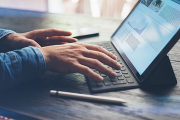 Man working at office.Closeup view of male hands typing on electronic tablet keyboard-dock station. Business text information on device screen. Horizontal side-view.