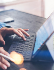 Closeup view of male hands typing on electronic tablet keyboard-dock station. Businessman working at office while sitting at wooden table.Vertical,cropped.Flares effect.