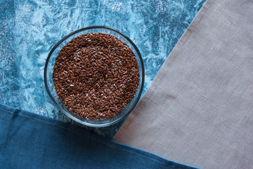 Superfood brown flax seeds in glass bowl on blue background. Bright colorful flat lay of healthy product.