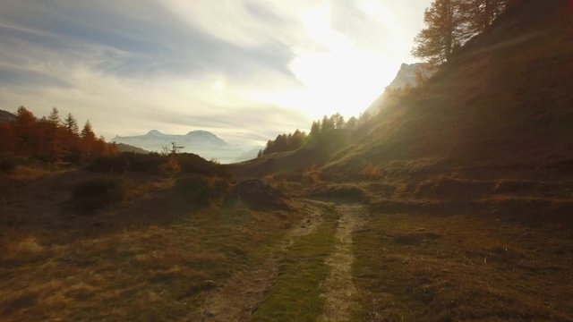POV walking on fall path to woods, valley and snowy mounts at sunset with sun flare.Sunny autumn day Hiking in colorful red forest wild nature mountain outdoors.4k point of view establishing video