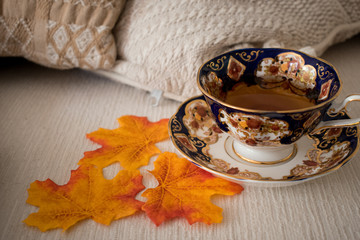 Cup of tea with autumn leaves in cozy environment with ivory and white cushions