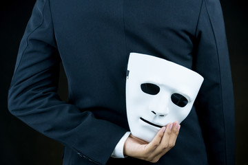 businessman hide the white mask in the hand behind his back on black background.