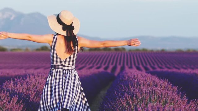 Happy Young Woman Enjoying Life in Lavender Field at Sunset. SLOW MOTION 120 FPS. Joyful girl in a summer dress dancing in endless blooming lavender fields.  Plateau du Valensole, Provence, France.