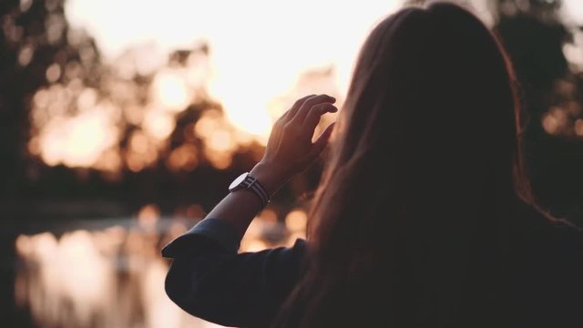 Woman looks at the Sun Shining through her Fingers. Slow Motion 120 fps, 4K.  Female hand Reaches for Sun, Touching the Light. Hope and Happiness Concept. 
