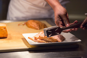 Chef picking the cutting or slicing piece of pork from wooden board to put on plate in hotel food restuarant,Professional cuisine concept