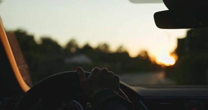 Man Driving a Car at Sunset. SLOW MOTION 4K DCi. Male Hand on steering wheel close up. Beautiful Road in blurred background.