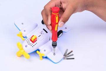 A hand holding a screwdriver to repair a toy.  White background.