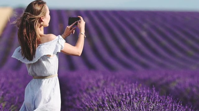 Woman Making Pictures of Endless Lavender Fields on a Smartphone. SLOW MOTION 120 fps. Beautiful Young Female Model using Phone to take Photos of Provence Nature. Plateau du Valensole, South France.