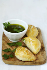 Empanadas with chimichurri sauce on wooden cooking board