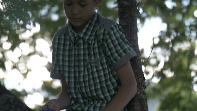 serious ruffian boy sitting on a tree waving legs and twirling spinner