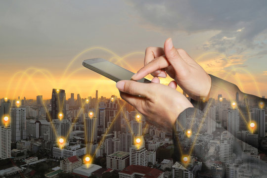 Double exposure of woman hand touch screen smartphone, mobile with pin flat above cityscape, sunset and glowing networking connection as business, technology and communication concept