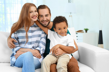 Happy couple with adopted African-American boy sitting on couch at home