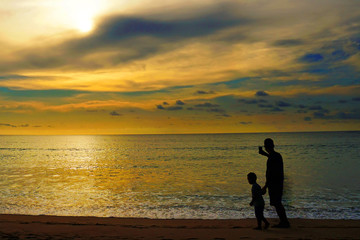 Fototapeta premium Silhouette of Dad and kid over sunset on summer ocean