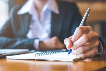 business woman hand working in a laptop computer is writing on notepad with a pen in office.