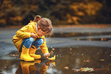 Obraz premium happy child girl with umbrella and paper boat in puddle in autumn on nature