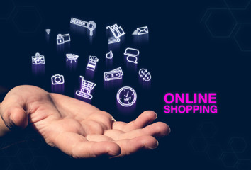 Online shopping pink word and glowing icon floating over open hand on dark blue background,e-commerce concept.