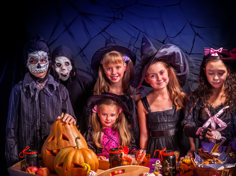 Halloween kids holding carved pumpkin as jack-o-lantern with trick or treat food at table. Black net with bat background.