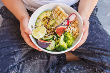 buddha bowl with tofu, broccoli and vegetables in the hands of a child