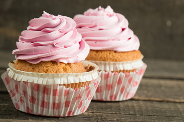 Closeup of cupcakes with vanilla, berries, pink and white cream, chocolate and sprinkles on wooden background. Selective focus. Sweet dessert tasty food concept muffin.