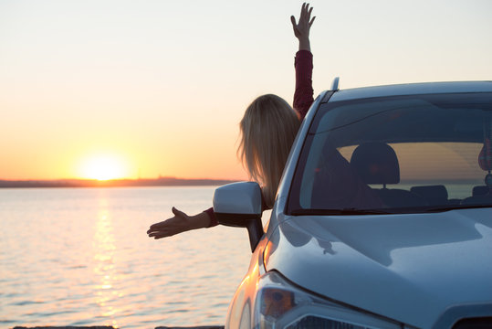 A young woman looks out the car window at the sunset on the sea.