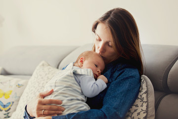 Young mother, kissing her newborn baby boy at home