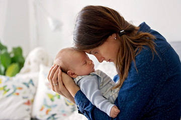 Young mother, kissing her newborn baby boy at home