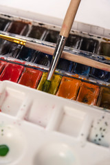 Close up of watercolor paints in bucket and white paper