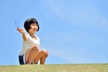 芝生広場でシャボン玉遊びをする女の子(青空)