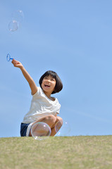 芝生広場でシャボン玉遊びをする女の子(青空)