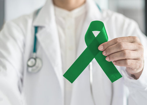 Jade (emerald) green ribbon in doctor's hand for Liver Cancer and hepatitis B awareness concept .