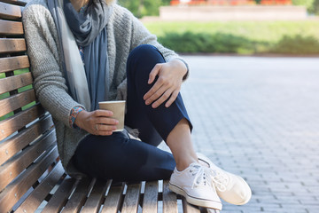 Woman is sitting on the bench and holding coffee.