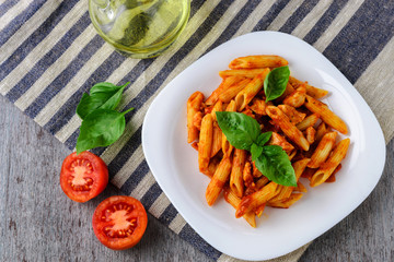 Penne with tomato sauce and basil on wooden background