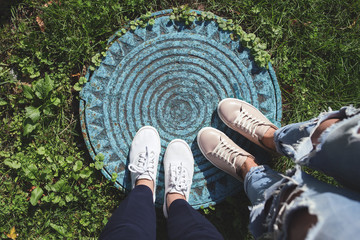 Two pairs of woman's legs, blue manhole, grass. Top view.