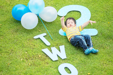 Closeup happy asian kid lie on grass floor in park textured background in 2 nd years anniversary...