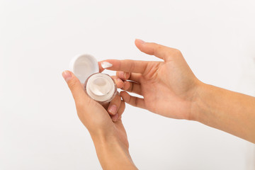 white cream in a small glass jar in female hands.