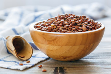 Dry brown lentils in a wooden bowl.