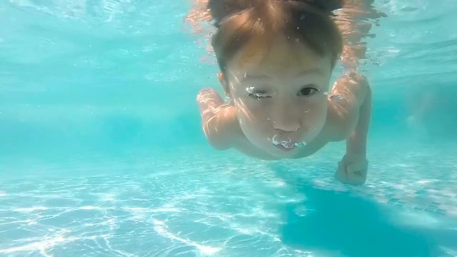 Cute little boy dives in blue pool with open eyes and swimming underwater in shallow water. Slow motion swimming boy underwater in pool