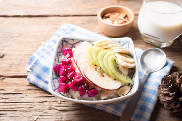 Bowl of oatmeal porridge with bananas, apple, dragon fruit and almonds. Top view