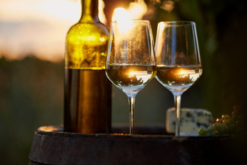Two glasses of white wine and bottle with food at sunset