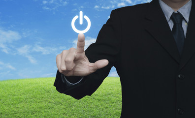 Businessman pressing power button over green grass field with blue sky, Start up business concept
