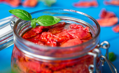 Sun dried tomatoes with basil in a glass jar on a blue wooden table. Vegetarian concept