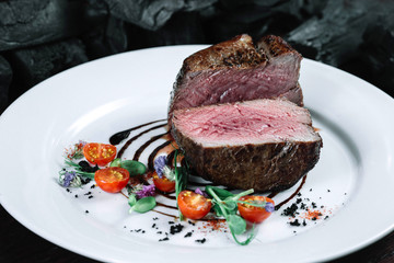 Tenderloin steak on plate with salad on dark background