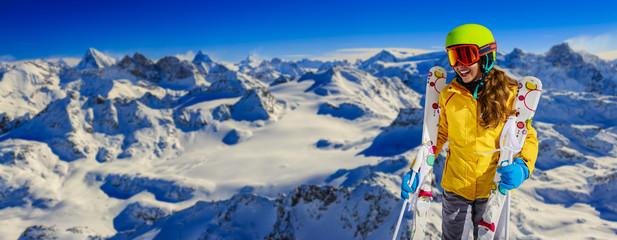 Skier teenager along a snowy ridge with skis. In background blue sky and shiny sun and Swiss Alps. ...