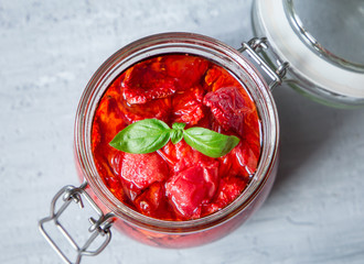 Sun dried tomatoes with basil in a glass jar on a concrete table. Vegetarian concept