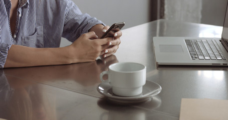 Blond model in a relaxed button-up shirt switches between her laptop and her phone