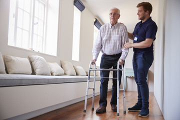 Senior woman using a walking frame with male nurse at home - obrazy, fototapety, plakaty