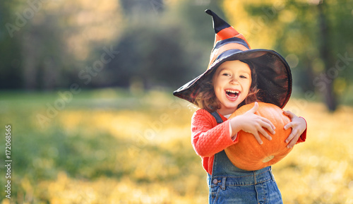 child girl with pumpkin outdoors in halloween