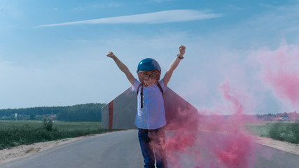 Little boy wearing helmet and styrofoam wings standing on a rural road, pretending to be a pilot