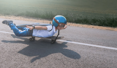 Little boy wearing helmet and styrofoam wings riding skateboard on a rural road, pretending to be a pilot © supamotion