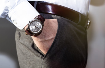 Closeup fashion image of luxury watch on wrist of man.body detail of a business man.Man's hand in a grey shirt with cufflinks in a pants pocket closeup. Tonal correction.